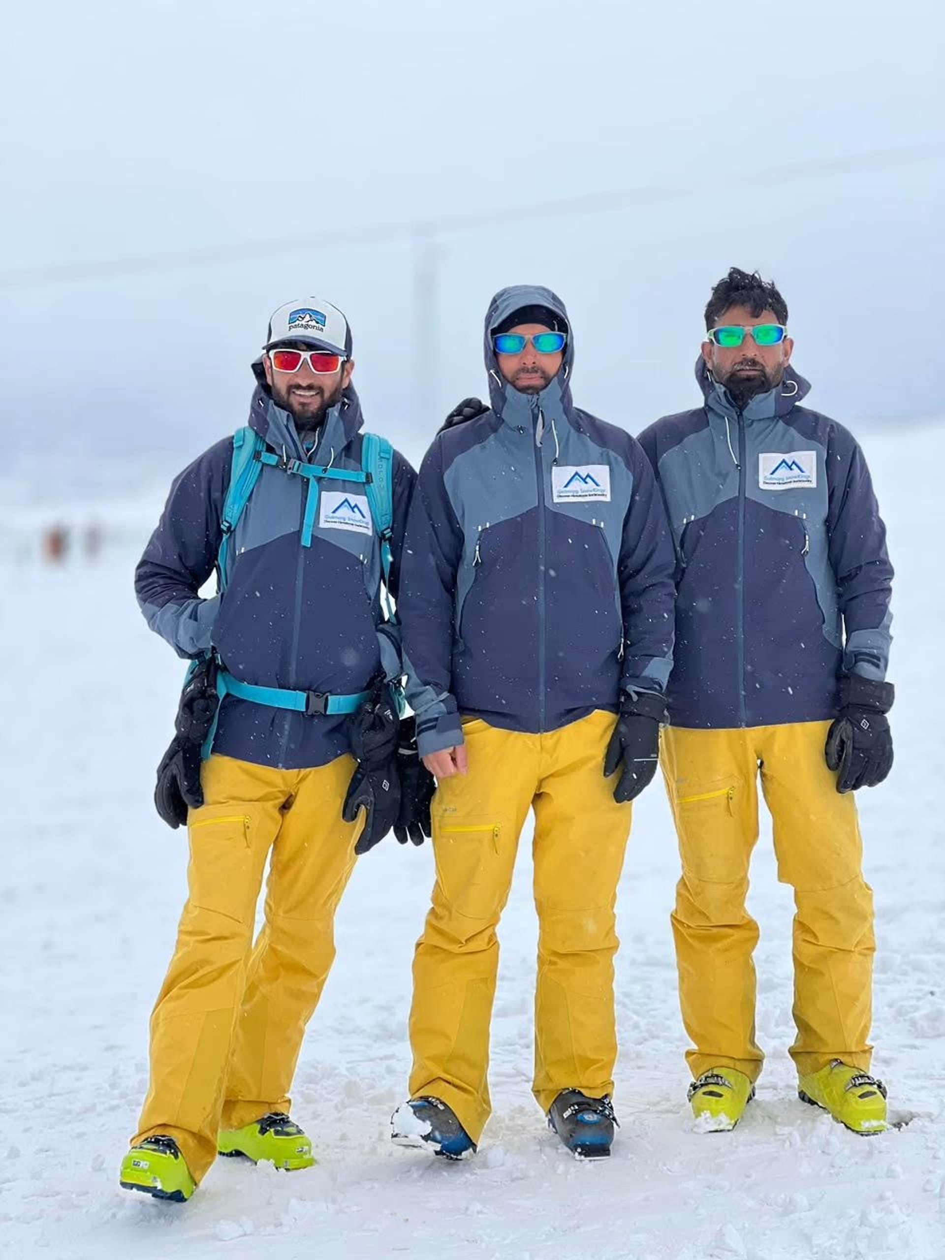 Three Gulmarg Snowkings guides in matching branded navy jackets and yellow trousers standing together on the snow.