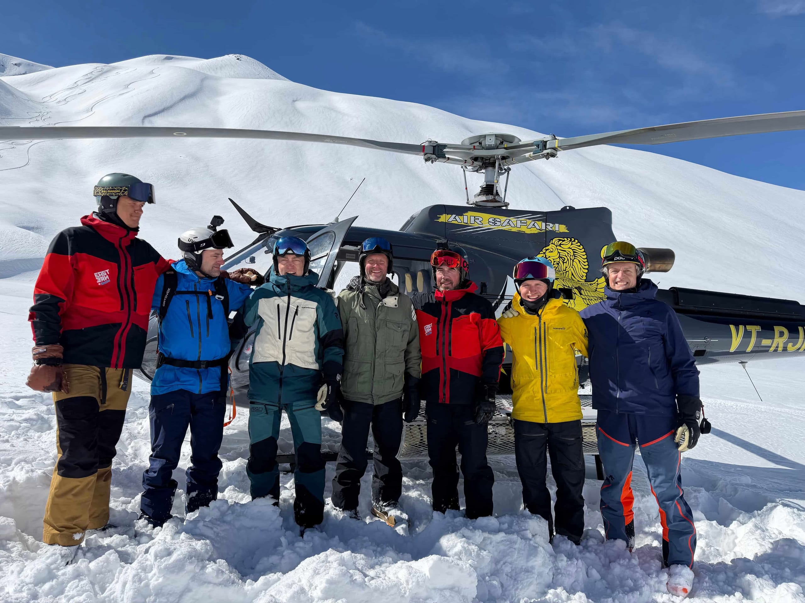 A group of skiers standing in front of a helicopter on a snow covered landing area.