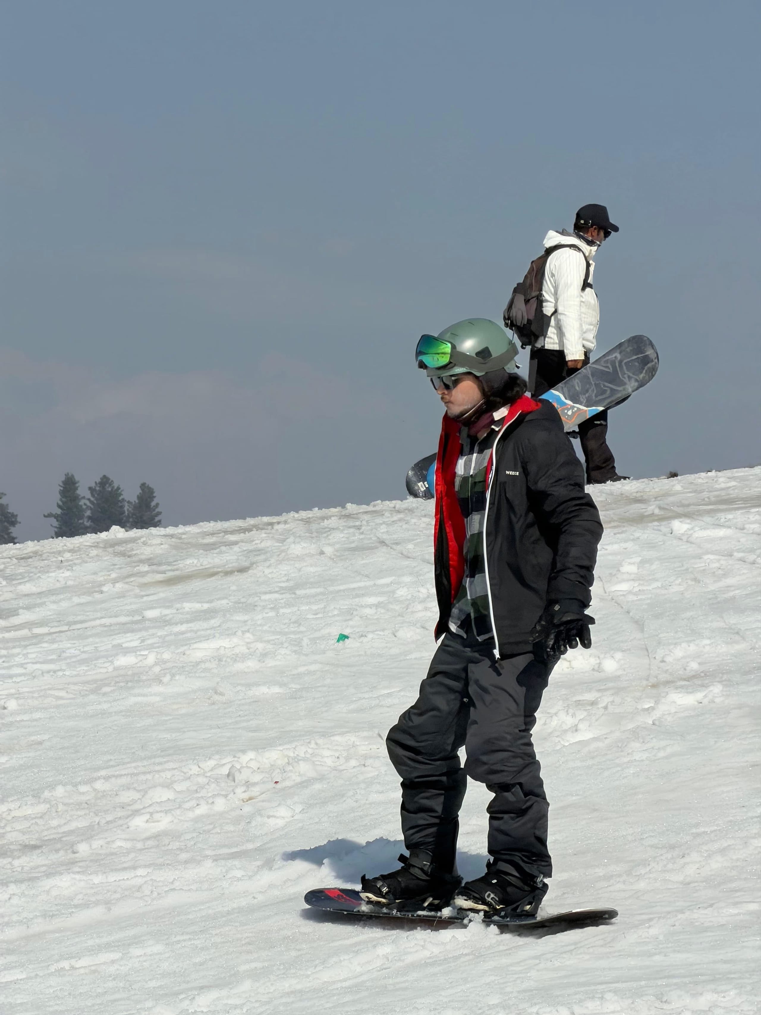 A snowboarder in a helmet standing on a gentle snow slope holding their board.