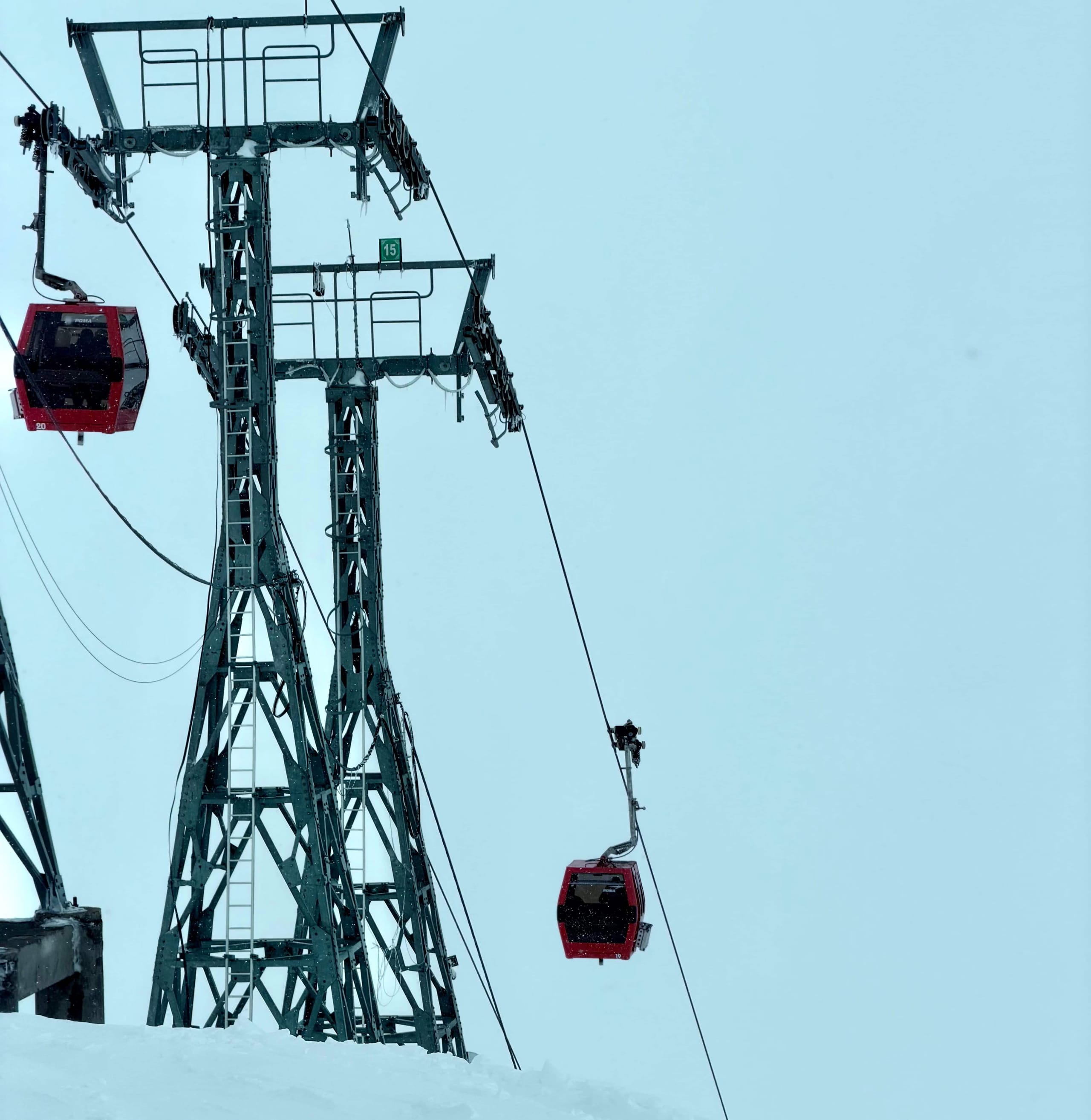Red Gulmarg gondola cabins on the cable beside a steel pylon against a pale winter sky.