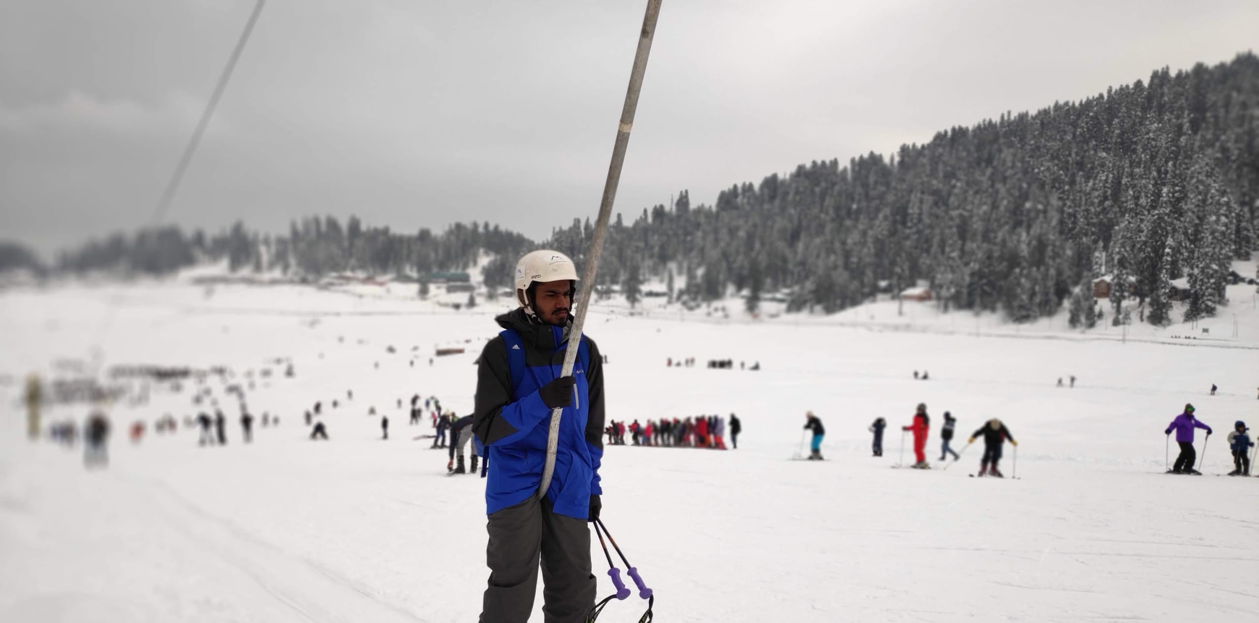 Skiers on an open groomed slope in Gulmarg with forested slopes behind.
