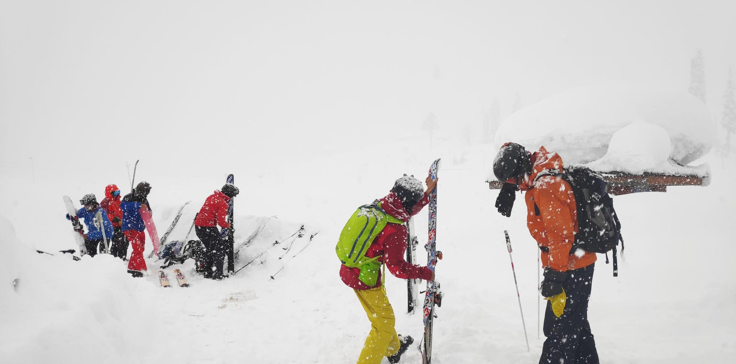 A group of skiers adjusting their equipment on a snowy slope during heavy snowfall.